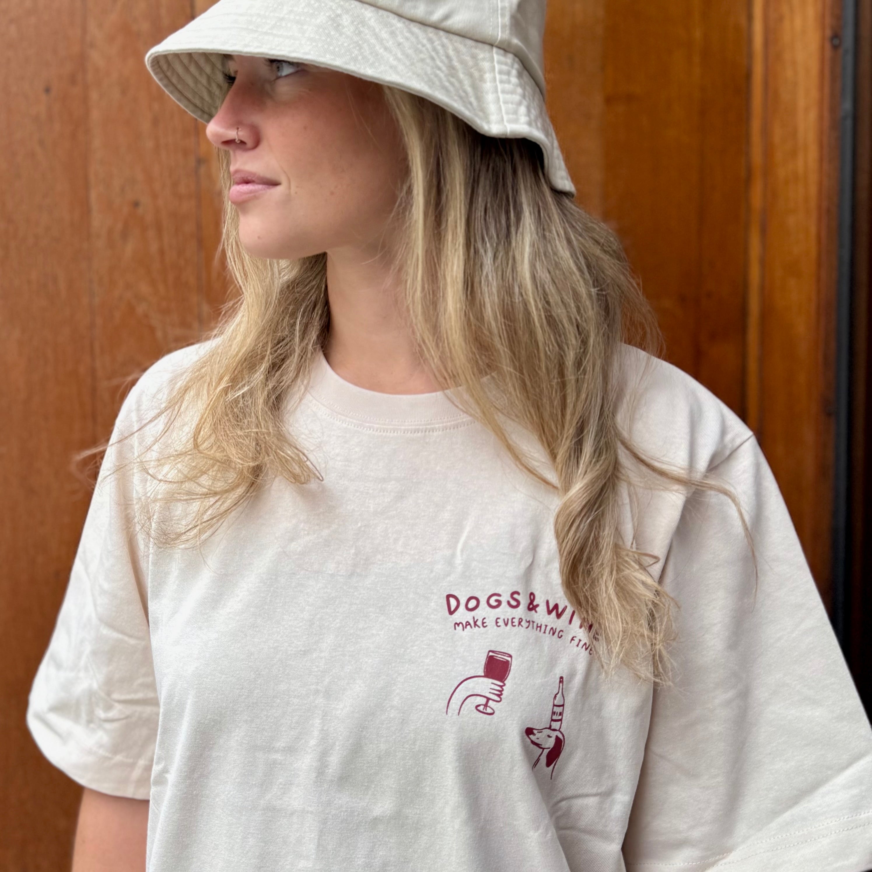 Person wearing a white t-shirt with a logo and text, standing against a wooden door.